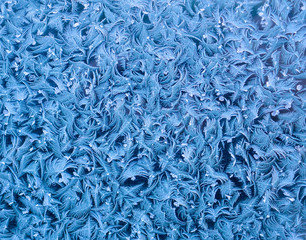 beautiful festive frosty pattern of ice with white snowflakes on a blue background on glass