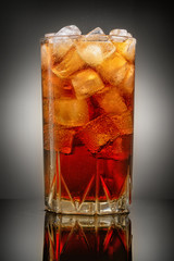 glass of Cola with ice on grey background with reflection