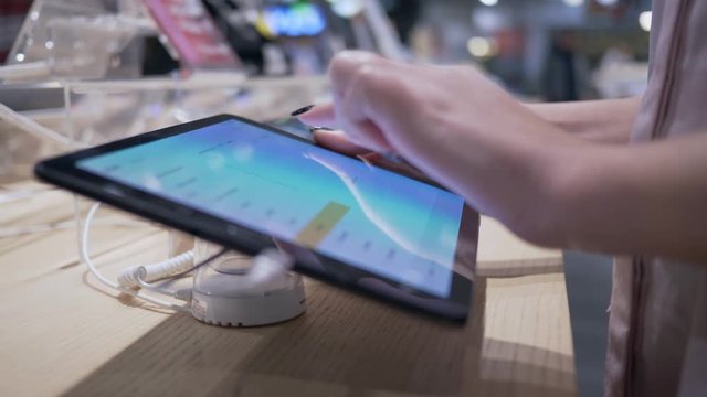 testing gadget, girl client uses modern tablet computer with touch screen at electronics store