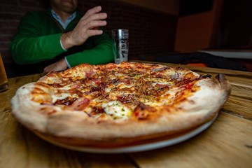 A delicious meat pizza sliced and ready to be eaten, with a person on the background