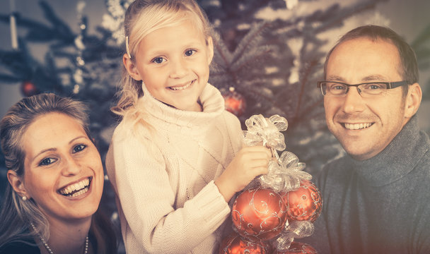 Young girl helping her family decorating the Christmas tree holding baubles in hand