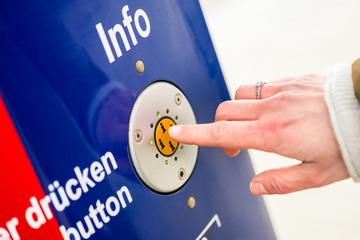 Woman pressing info button of assistance machine in train station, only finger to be seen