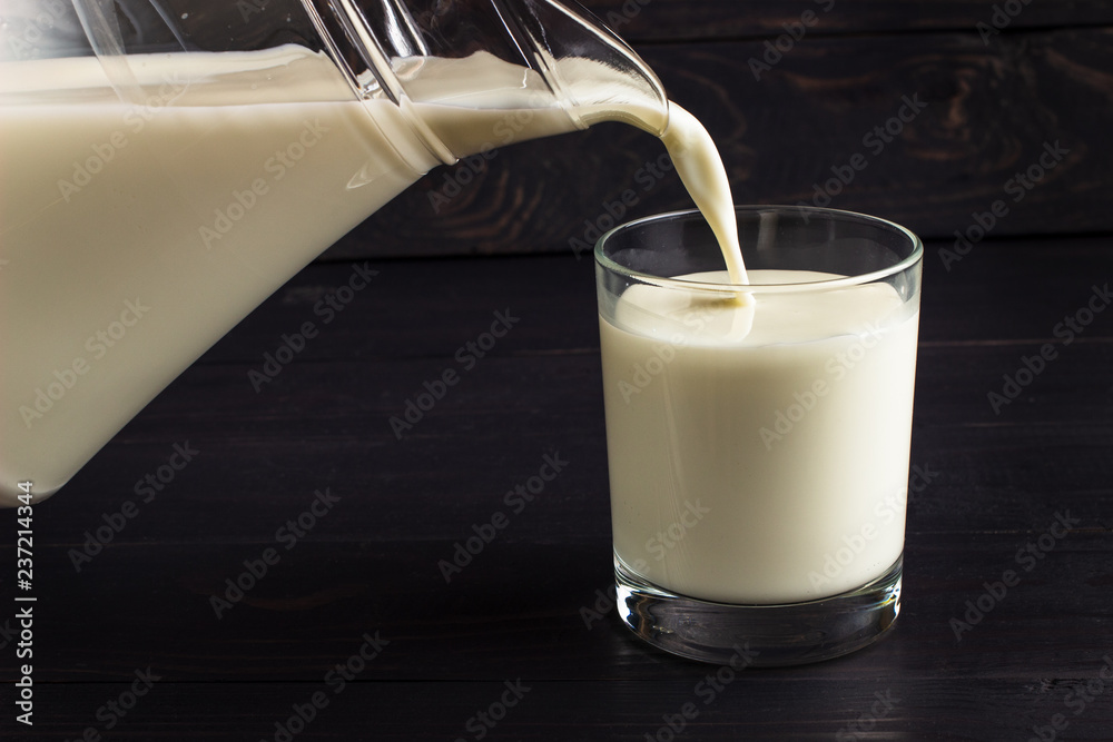 Wall mural Pour milk into a glass on a dark background