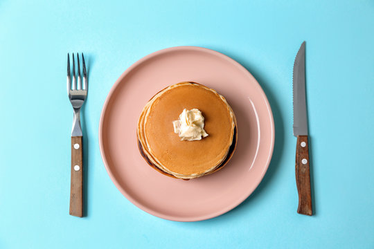 Plate with hot tasty pancakes and butter on color background