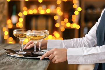 Waiter putting tray with glasses of champagne onto table against defocused lights