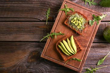 Wooden board with delicious avocado toasts on table, top view
