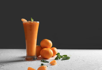 Glass of tasty orange smoothie and tangerines on white table