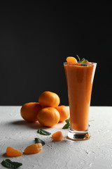 Glass of tasty orange smoothie and tangerines on white table