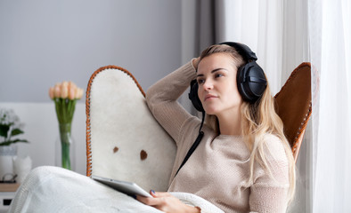 Woman at home wearing headphones while using digital tablet, listening to audiobooks or music