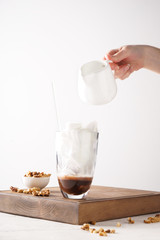 Woman pouring coffee into glass with ice cubes on wooden board