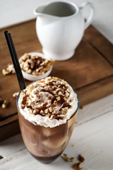 Glass of tasty cold coffee with walnuts on white wooden table