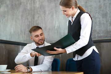 Young waitress showing man a menu in restaurant
