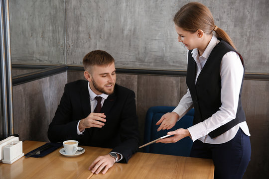 Young waitress with menu on tablet PC screen in restaurant
