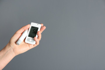 Woman holding digital glucometer and lancet pen on grey background. Diabetes control