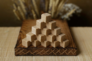 Cubes of brown sugar on the kitchen table. Rustic still life with wooden and glass utensils.