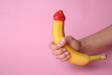 Woman holding banana with strawberry on color background. Erotic concept - obrazy, fototapety, plakaty