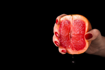 Woman squeezing half of juicy grapefruit on black background. Erotic concept