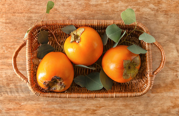 Wicker basket with ripe persimmons on wooden table, top view