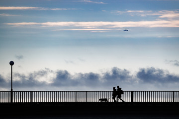 People in silhouette standing on a bridge over a sea