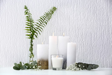 Beautiful composition with burning candles on table near white wall