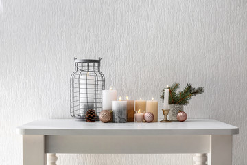 Christmas composition with burning candles on table near white wall