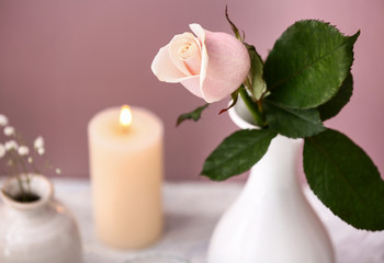 Fototapeta na wymiar Beautiful rose in vase and blurred burning candle on background