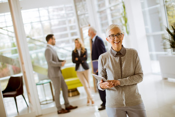 Portrait of senior businesswoman with digital tablet while other business people standing in background