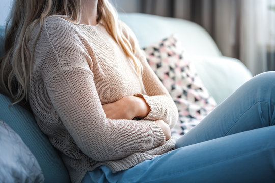 Young woman suffering from abdominal pain while sitting on sofa at home