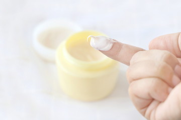 Side view of close up woman finger applying cream in jar on white fabric background