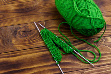 Ball of yarn and knitting needles with knitting on wooden table