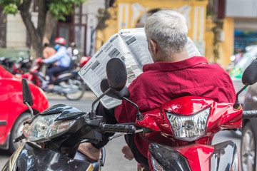 unrecognizable man in red shirt reads newspaper, sits on the sco