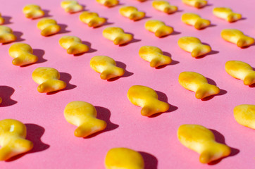Cookies in form of fish on a pink background in bright light with hard shadows.