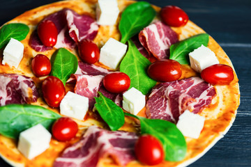 pizza with ham, whole tomatoes and cheese, basil on wooden background