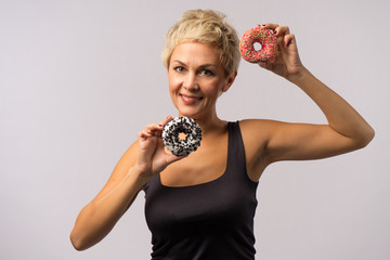 Beautiful mature woman is holding two bright donuts in hands.