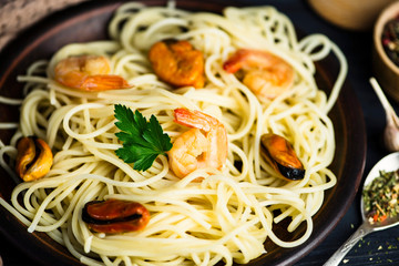 spaghetti with seafood in a plate and spices on a wooden board