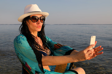Pretty Woman Enjoying Her Summer Holiday, Sitting On The Rocks By The Sea And Taking Selfie On Sunny Summer Day 