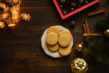 Christmas atmosphere flatlay on wooden background. Cookies, candies, electric garland and golden decorations