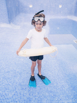 Boy in diving equipment with lifebuoy in empty pool