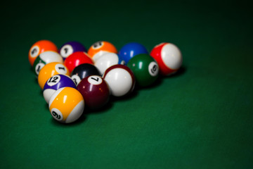 Sport billiard balls set arranged in shape of triangle on green billiard table in pub. Players are ready for the first hit of the round to start the billiard game.