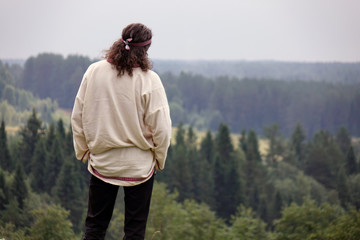 A young man in a traditional folk costume in nature, looking into the distance. Green pine forest.