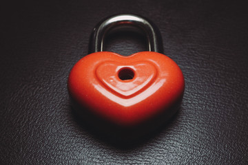 Metal red lock in the shape of the heart on black skin. Abstract love background.