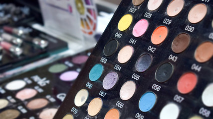 Stand with bright colored tester eye shadow samples in beauty store. Makeup shop, mineral shadow, eye shadow palette background. Woman chooses eyeshadow