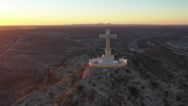 A Christian cross on a monument on top of a mountain at sunset