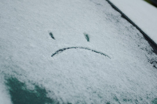 sad smiley painted on the car window with a finger in the winter.