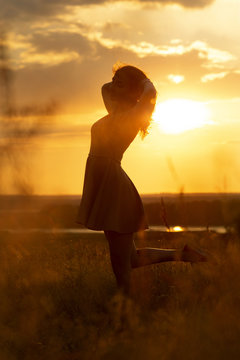 silhouette of a beautiful girl in a dress at sunset in a field, figure of young woman enjoying nature, concept of leisure