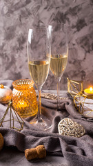 Two glasses with champagne on a gray background among gold Christmas and New Year decorations and candles. Home holiday mood concept