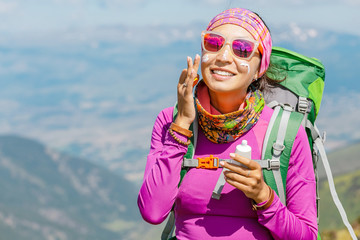 Hiker woman applying sun cream to protect her skin from dangerous uv sun rays high in mountains....