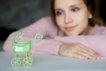 Young pretty girl looks hopefully and tenderness at a pram toy. The stroller in the foreground, a woman in the blur blurred. Desire to become a mother,  The stroller is on the left