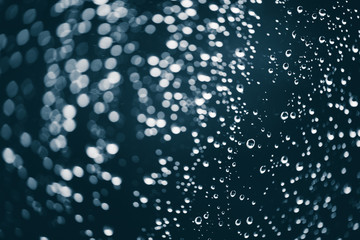 Dirty window glass with drops of rain. Atmospheric blue background with raindrops in bokeh. Droplets and stains close up. Detailed transparent texture in macro with copy space. Rainy weather.