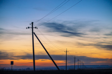 Power lines in field on sunrise background. Silhouettes of poles with wires at dawn. Cables of high...
